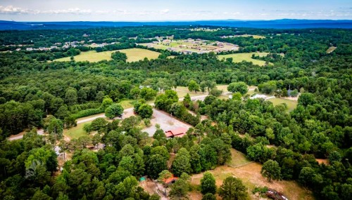 Aerial view of lush green fields and wooded areas, with a small red building amidst the landscape.
