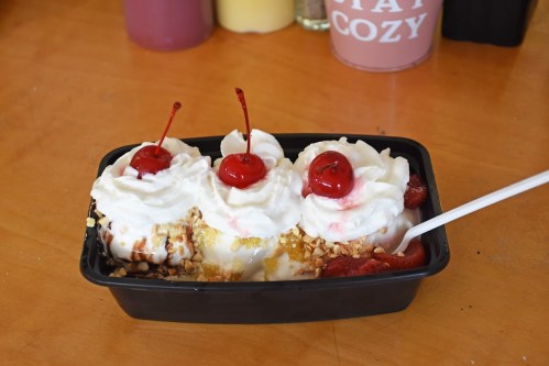 A dessert bowl with three scoops of ice cream topped with whipped cream, nuts, and cherries.