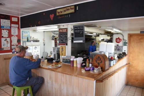 A diner interior with a man sitting at the counter, enjoying a meal, surrounded by colorful decor and menu boards.