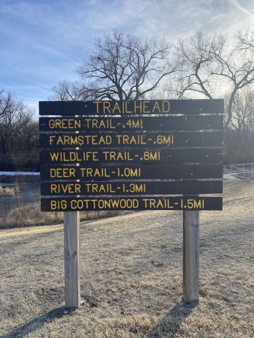 Trailhead sign listing various trails and their distances: Green Trail (4 mi), Farmstead Trail (0.6 mi), Wildfield Trail (0.8 mi), Deer Trail (1.0 mi), River Trail (1.3 mi), Big Cottonwood Trail (1.5 mi).
