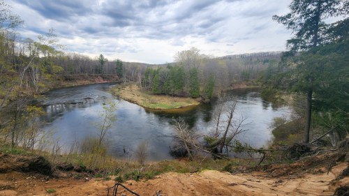 A scenic view of a winding river surrounded by trees and hills under a cloudy sky.