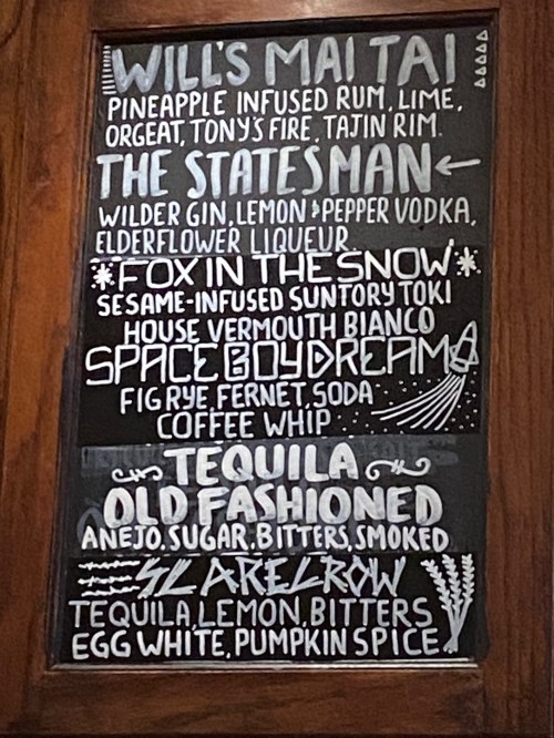 Menu board featuring cocktail names and ingredients, including Mai Tai, Statesman, Fox in the Snow, and more.