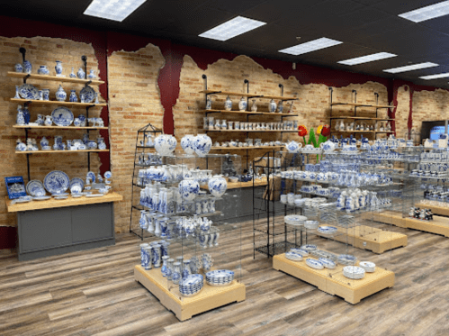 A store interior displaying various blue and white ceramic items on shelves and glass displays against a brick wall.