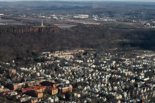 Aerial view of a town with dense housing, a river, and a prominent cliff with a monument in the background.