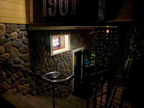 A dimly lit staircase leading down to a stone-walled entrance with a window and decorative lights.