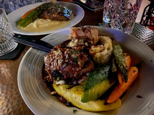 A plate of grilled meat with mashed potatoes and assorted vegetables, including zucchini, carrots, and asparagus.