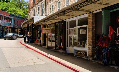 A street view featuring shops, including Wobbles Eatery, with people walking and a car parked nearby.