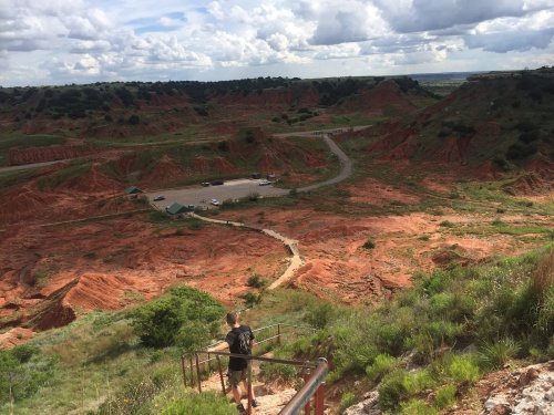 A person descends a staircase overlooking a vast, red rock landscape with scattered clouds in the sky.