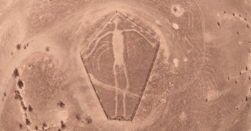 Aerial view of a large geoglyph resembling a human figure, set in a barren landscape.