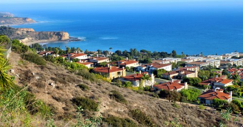 A coastal view of upscale homes overlooking the ocean, with cliffs and greenery in the foreground.