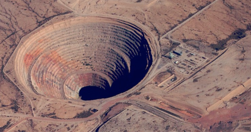 Aerial view of a large, circular open-pit mine surrounded by arid land and small structures.