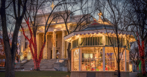 A festive gazebo adorned with lights, set against a historic building decorated for the holidays.