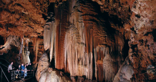 Visitors explore a cave with impressive stalactites and stalagmites, illuminated by soft lighting.