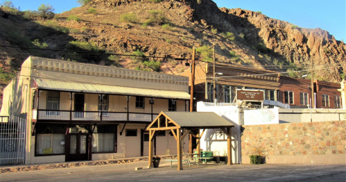 Historic buildings with a mountain backdrop, featuring a wooden gazebo in the foreground and clear blue skies.