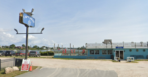 A seaside restaurant with a blue exterior, outdoor seating, and a sign reading "Captain's." Parking area visible.