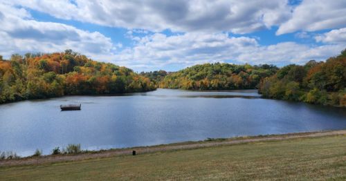 A serene lake surrounded by colorful autumn trees under a partly cloudy sky.