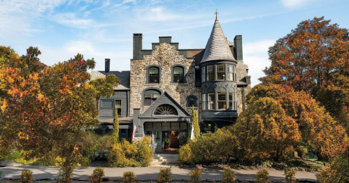 A grand stone mansion with a turret, surrounded by colorful autumn trees and a clear blue sky.