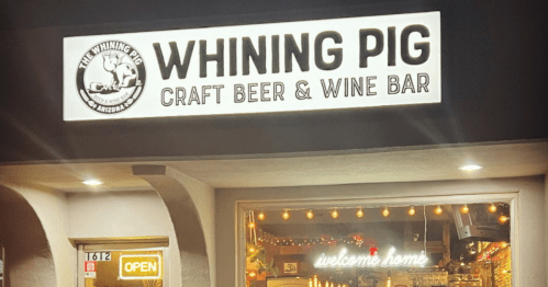 Sign for "Whining Pig Craft Beer & Wine Bar" with an open sign and warm lighting visible through the window.