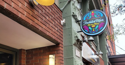 Sign for "Indita Mia" restaurant on a brick building, featuring colorful design and warm lighting.