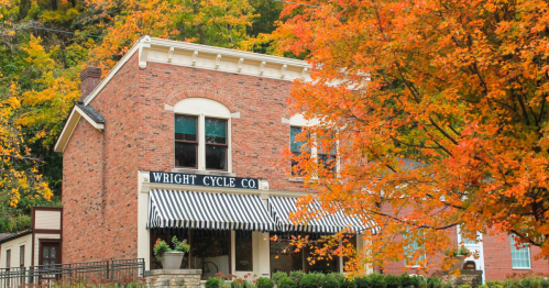 Historic brick building with "Wright Cycle Co." sign, surrounded by vibrant autumn foliage.