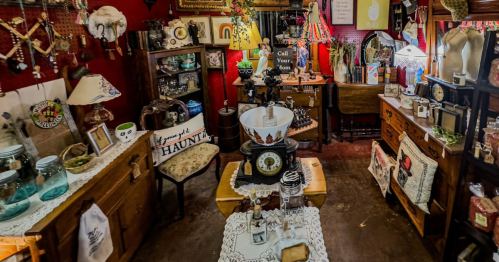 A cozy vintage shop filled with eclectic decor, antiques, and handmade items on wooden furniture against a red wall.