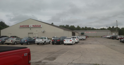 A large warehouse building with "Hancocks of Paducah" signage, surrounded by parked cars under a cloudy sky.