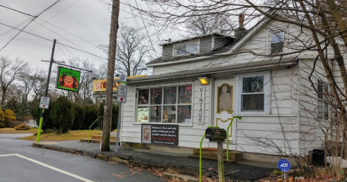 A vintage shop with a white exterior and green accents, located on a roadside with signs and trees in the background.