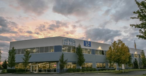 Exterior of a modern building with "Happyrock Beads" sign, surrounded by trees and a colorful sunset sky.