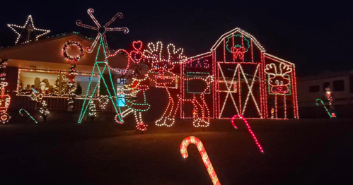 Colorful Christmas lights decorate a house, featuring reindeer, a barn, and candy canes against a night sky.