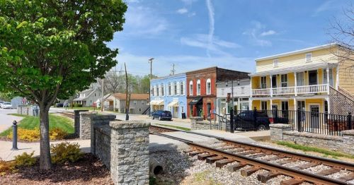 A quaint street with colorful buildings, a tree, and railroad tracks under a clear blue sky.