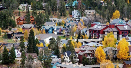 A scenic view of a colorful mountain town with autumn foliage and various houses nestled among trees.
