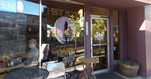 Exterior of New Moon Cafe with a large window, outdoor seating, and a person sitting at a table.