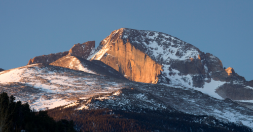 A majestic mountain peak bathed in golden sunlight, surrounded by snow-covered slopes and evergreen trees.