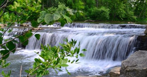 A serene waterfall cascades over rocks, surrounded by lush green trees and foliage.