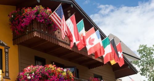 A colorful balcony adorned with flowers and various national flags, set against a blue sky.