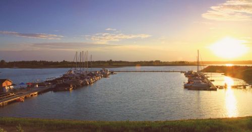 Sunset over a tranquil marina with boats docked, reflecting golden light on calm waters.