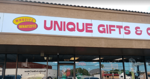 Sign for "Whozit Whatzit Unique Gifts & More" on a storefront, featuring bright colors and an open sign.