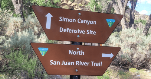 Brown directional sign indicating "Simon Canyon Defensive Site" and "North San Juan River Trail."