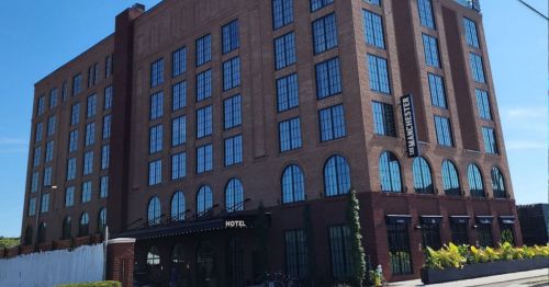 A modern brick hotel building with large windows and a sign reading "Winchester" on a clear day.