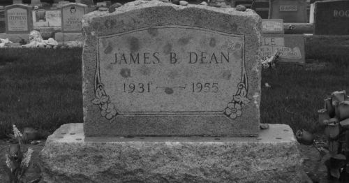 Gravestone of James B. Dean, engraved with his name and years of birth and death, surrounded by grass and flowers.