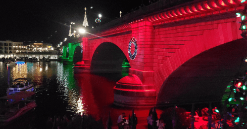A brightly lit bridge at night, adorned with red and green lights, reflecting in the water below.