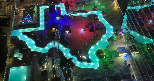 Aerial view of a vibrant pool shaped like Texas, illuminated with colorful lights and surrounded by lounge areas.