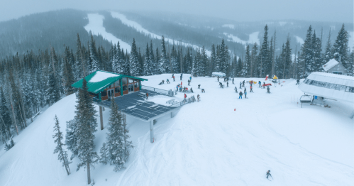 A snowy mountain landscape with a ski lodge, skiers, and snowboarders enjoying the slopes amidst tall pine trees.