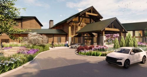 A modern lodge entrance surrounded by colorful flowers and greenery, with cars parked and people walking.