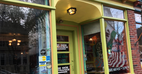 Colorful café entrance with a green door, open sign, and large windows displaying a vibrant interior.
