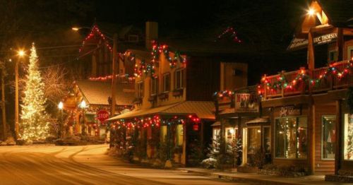 A festive street scene at night, adorned with Christmas lights and a decorated tree, creating a cozy holiday atmosphere.