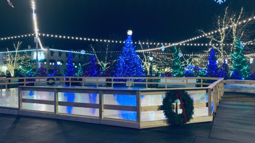 A festive outdoor ice skating rink surrounded by colorful holiday lights and decorated trees at night.