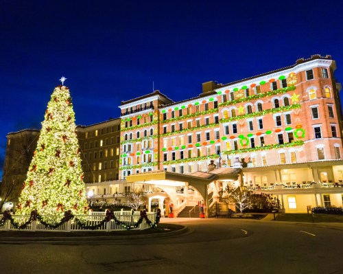 A beautifully lit hotel decorated for Christmas, featuring a large tree and festive lights against a night sky.