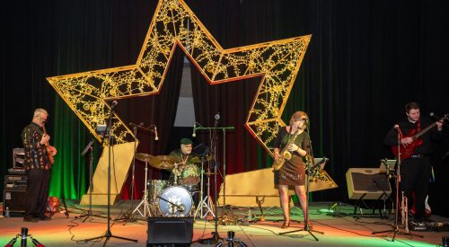 A band performs on stage in front of a large illuminated star decoration, with colorful lighting and musical instruments.