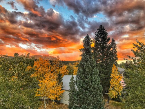 A vibrant sunset over a forest with colorful autumn trees and a house, creating a picturesque landscape.